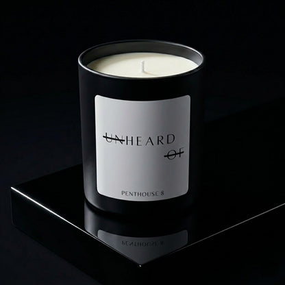 UNHEARD OF Penthouse 8 luxury candle, matte black jar with minimalist label, 8oz hand-poured coconut wax, smoky incense and charred birchwood scent, high-end editorial art piece.