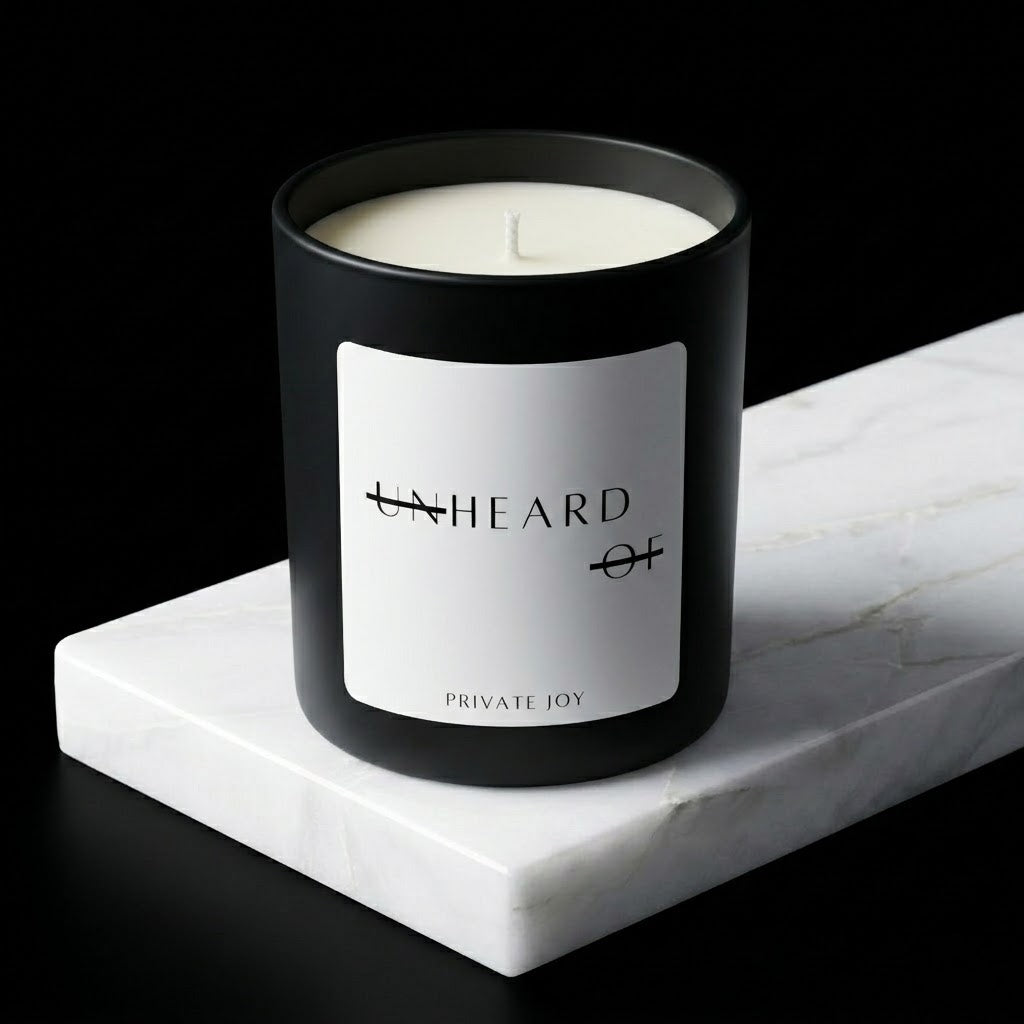UNHEARD OF Private Joy luxury candle, matte black jar with minimalist label, 8oz hand-poured coconut wax, almond milk and tonka bean scent profile.