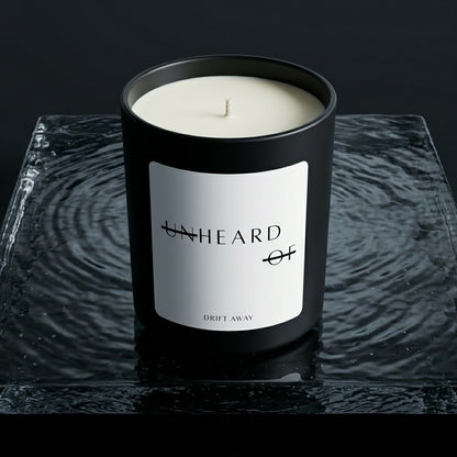 UNHEARD OF Drift Away luxury candle, matte black jar with minimalist label, 8oz hand-poured coconut wax, sea salt and driftwood scent profile.