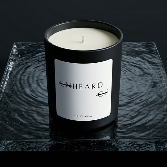 UNHEARD OF Drift Away luxury candle, matte black jar with minimalist label, 8oz hand-poured coconut wax, sea salt and driftwood scent profile.